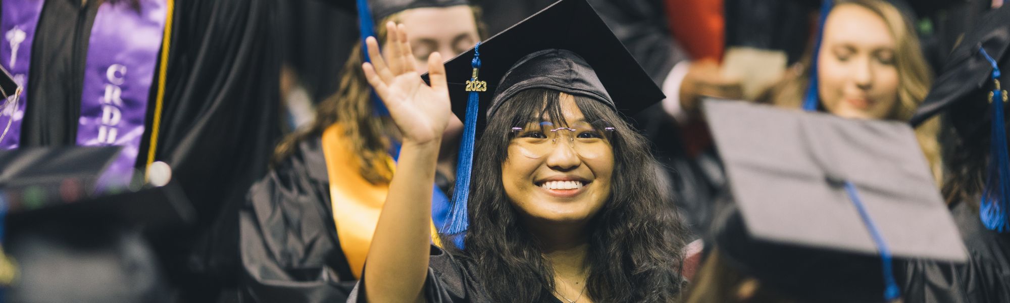 Female student in cap and gown smiling and waving