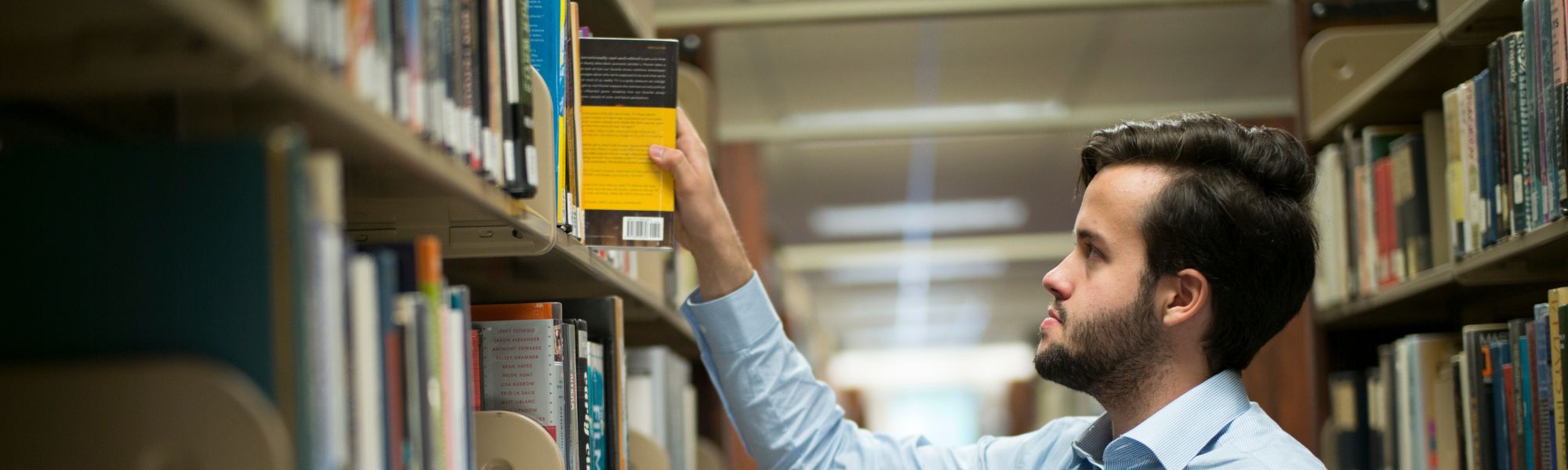 Student grabbing a book from a library shelf.